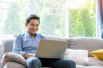 Young Asian men smiling while use internet on computer laptop  in the living room at home