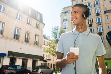 Wall Mural - happy young arabic man holding cellphone ion city and listening to music with headphones