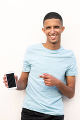 Wall Mural - smiling young arabic man holding mobile phone and pointing to screen by white background