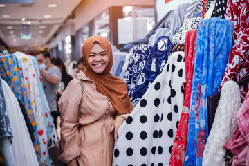 Wall Mural - Portrait of a gorgeous Hispanic fashion designer holding a roll of fabric in a workshop . Young muslim woman seller smiling and displaying white fabric at shop.