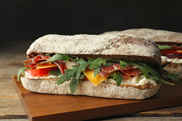 Delicious sandwich with fresh vegetables and prosciutto on wooden table, closeup