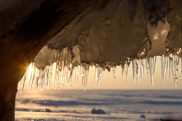 Wall Mural - icicles on the shore of a frozen lake at sunset.