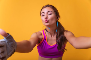 Wall Mural - Image of a positive young brunette sports fitness woman posing isolated over yellow background take selfie by camera and send air kiss, cute .Attractive girl making a selfie after her exercise.