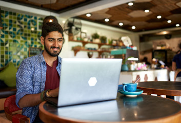 handsome millennial indian man working in trendy coworking space