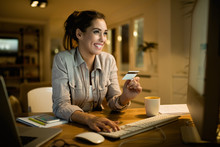 Happy Woman Using Credit Card For Online Banking At Night At Home.