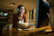 © Drazen - Happy woman eating popcorn and watching a movie on desktop PC at night.