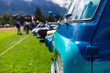 Old Vintage Classic American turquoise blue van car front, side view close up on the grass during an outdoor show, people and cars in the background