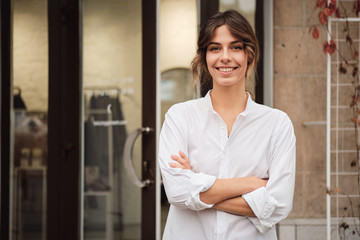 Wall Mural - Young beautiful woman holding hands crossed confidently looking in camera near showroom