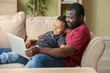 © Pixel-Shot - Portrait of African-American man and his little son with laptop at home