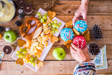 Couple of hands in top view taking two christmas sweet cakes on a wooden table with fruits and winter decorations - home party with family and friends together