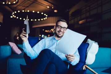 Wall Mural - Happy professional expert in spectacles reading text information from capital report and doing documents analyze indoors, cheerful businessman accounting capital strategy during working process