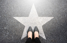 Success In Business Design Concept. Businesswoman Standing On Street Road Background. Top View. Selfie Of Feet In Black High Heels Shoes And White Star Symbol On Pathway Floor. New Talent Or Champion.