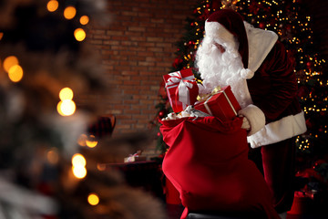 Poster - Santa Claus packing gifts into bag near Christmas tree