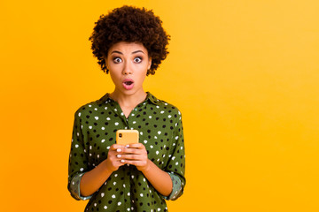 Poster - Photo of beautiful shocked dark skin wavy lady open mouth hold telephone read advert unbelievable big shopping prices wear green dotted shirt isolated yellow color background