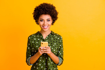 Portrait of positive cheerful afro american girl social network addicted user hold smartphone read social media news wear stylish clothes isolated over shine color background