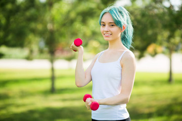 beautiful young woman goes in for sports with dumbbells in the summer in the park