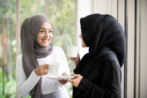 Fotografía Two Asian Muslim woman standing and talking in the office with a cup of coffee