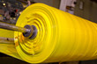 © josh - Yellow spool of plastic packaging sheet heavy duty for industrial use outdoors. wrapped around a worn metal pole ready to feed into a machine for cutting into shape or printing logos or branding.