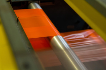 image of the inside workings of a machine with orange high vis plastic sheet being fed through industrial factory on rollers with tension keeping it straight being stretched and cut ready for packing