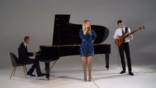Girl sings in trio with piano player and bass guitarist in blue dress