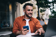 © BullRun - Cheerful man using gadgets in outdoors cafeteria