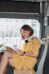 Wall Mural - Young woman reading book while moving in the modern tram, happy passenger at the public transport