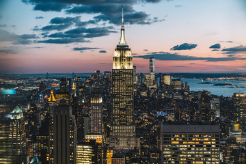 Wall Mural - Aerial view of skyscrapers and towers in midtown skyline of Manhattan with evening sunset sky. Scenery cityscape of financial district with famous New York Landmark, illuminated Empire State Building