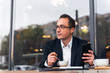 © Petryshak - Businessman in outdoor cafe drinking cup of coffee while using mobile phone, with copy space.