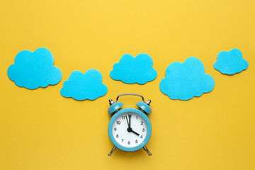 Wall Mural - Blue round alarm clock and clouds on the yellow background.