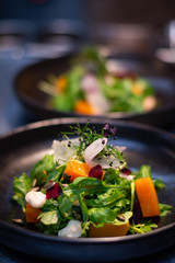 Vegetarian salad with fresh herbs, beetroot, pumpkin, radish and salad, served with olive oil on black plate in a restaurant