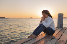The Girl Sits In Prayer To God With A Promise. With Love For God At Sea Ocean Outdoors During The Sunset In The Winter