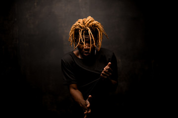 Wall Mural - Black guy with blonde dreadlocks posing in the dark outfit with the emotional face in action