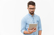 © Mangostar - Serious entrepreneur checking email on tablet. Handsome young man in casual shirt and glasses standing isolated over white background. Wireless internet technology concept