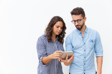 Serious focused couple reading message on tablet screen. Young woman in casual and man in glasses in glasses posing isolated over white background. Concerning news concept