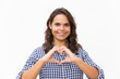 © Mangostar - Happy friendly student girl making heart shape with hands and fingers. Young woman in casual checked shirt standing isolated over white background. Love or healthcare concept
