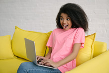 Excited African American Woman Using Laptop Computer And Fast Internet Connection, Sitting On Sofa, Watching Movie. Beautiful Curly Haired Girl With Emotional Face Shopping Online, Ordering Food