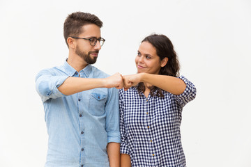 Satisfied couple making fist bump gesture. Young woman in casual and man in glasses standing isolated over white background. Cooperation concept