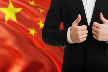 China businessman showing thumbs up behind country flag with copy space. Successful international relations and agreement concept.