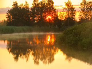 Wall Mural - backlit landscape, sunrise by the lake. the mist rises above the water, the foreground of the lake blurred