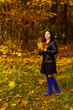 © finist_4 - A young brunette woman in blue boots is walking in an autumn park with yellow leaves in her hands