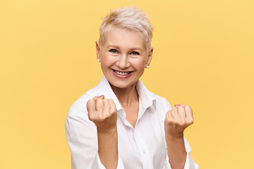 Isolated image of strong independent European businesswoman with short dyed hair expressing positive attitude, smiling confidently, clenching fists. Women, femininity, power, confidence and success