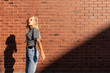 © Vasya - Attractive blonde teen girl in grey striped y-shirt and jeans touching her hair and lookinf at the camera isolated over red brick wall