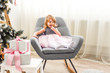 © Uliana - beautiful girl in a pink dress sitting on a chair near a Christmas tree