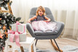 © Uliana - beautiful girl in a pink dress sitting on a chair near a Christmas tree