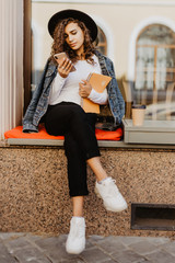 Wall Mural - Young pretty woman wearing in hat use mobile phone while sitting on the bench in cafe