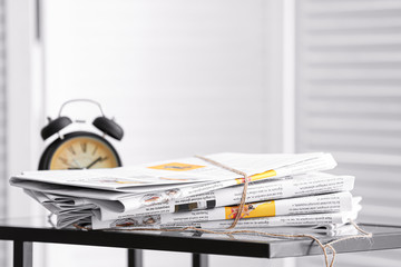 Stack of newspapers and clock on table in room