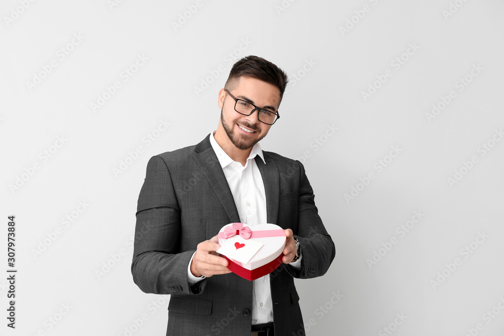 Handsome man with gift on light background. Valentine's Day celebration