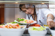 Medical doctor bent over with a salad plate picking up food at a self-service restaurant