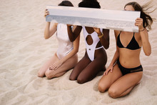 Three Female Models Sitting On Ocean Shore Holding Large Mirror, Reflections Of The Sea Beach. Travel Concept, Dream Of Summer Vacation
