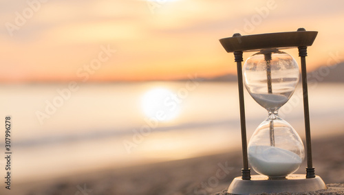 Hourglass in the dawn time. Sand passing through the glass bulbs of an hourglass measuring the passing time as it counts down to a deadline or closure on a sunset/ sunrise beach background.